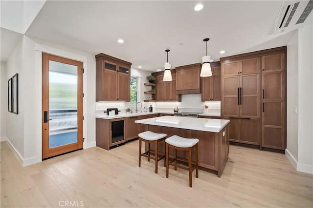 kitchen featuring premium range hood, hanging light fixtures, a kitchen breakfast bar, a center island, and light wood-type flooring