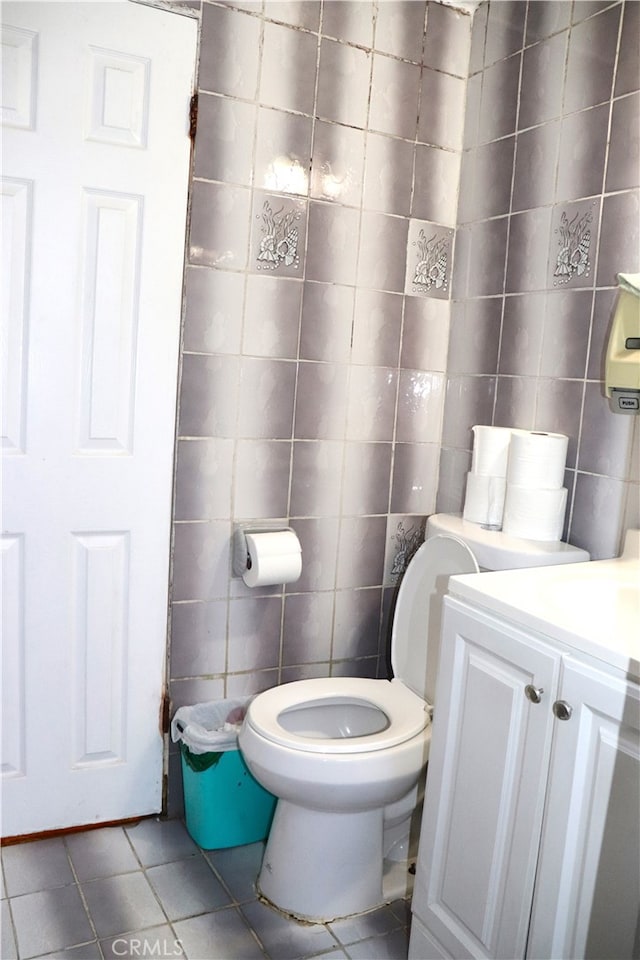 bathroom with toilet, vanity, tile patterned floors, and tile walls