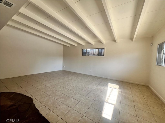 empty room with beam ceiling, light tile patterned flooring, and a healthy amount of sunlight