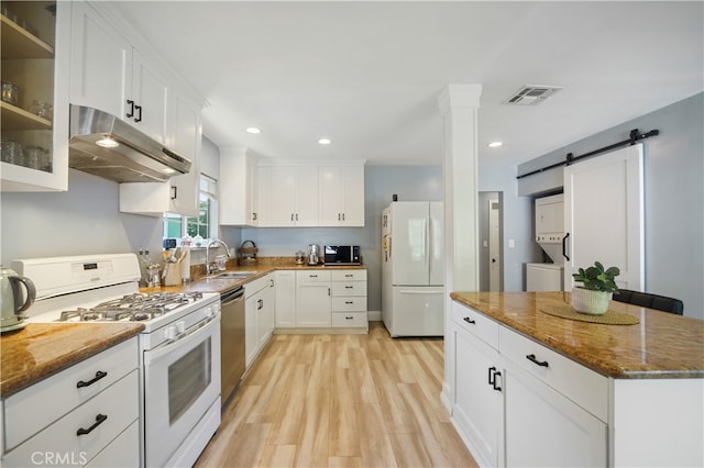 kitchen featuring white cabinets, white appliances, stone countertops, stacked washing maching and dryer, and a barn door