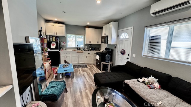 kitchen with white cabinets, black appliances, light hardwood / wood-style floors, and a wall mounted AC