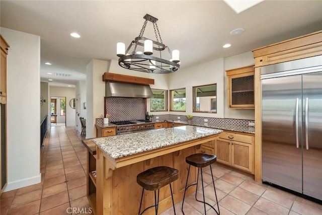 kitchen featuring high quality appliances, backsplash, light stone countertops, range hood, and a kitchen island