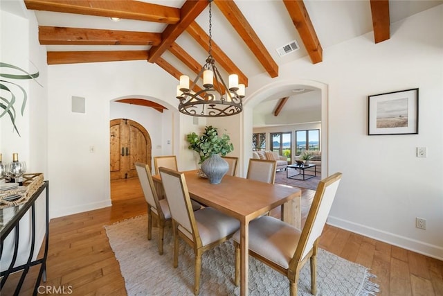 dining room with a chandelier, lofted ceiling with beams, and light wood-type flooring