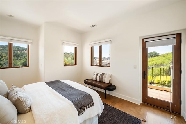 bedroom with access to exterior, light wood-type flooring, and multiple windows