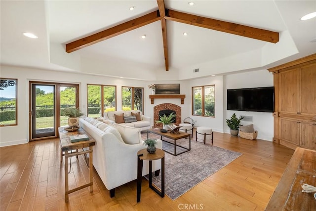 living room with a fireplace, beam ceiling, light wood-type flooring, and plenty of natural light