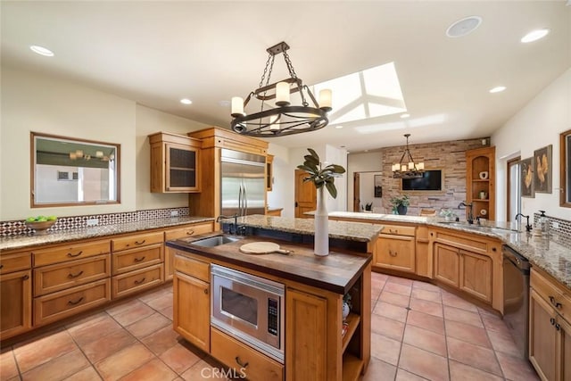 kitchen featuring kitchen peninsula, a skylight, built in appliances, a center island with sink, and hanging light fixtures