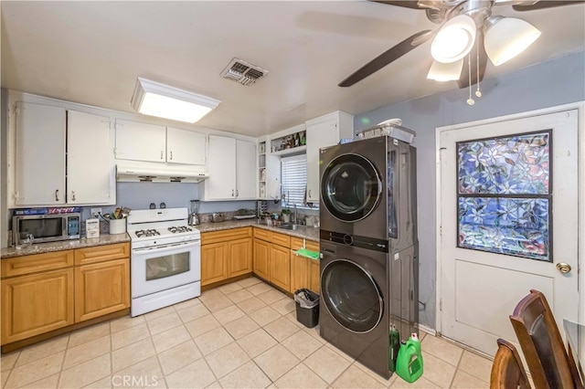 kitchen with white cabinets, light tile patterned floors, stacked washer / drying machine, white range with gas cooktop, and ceiling fan