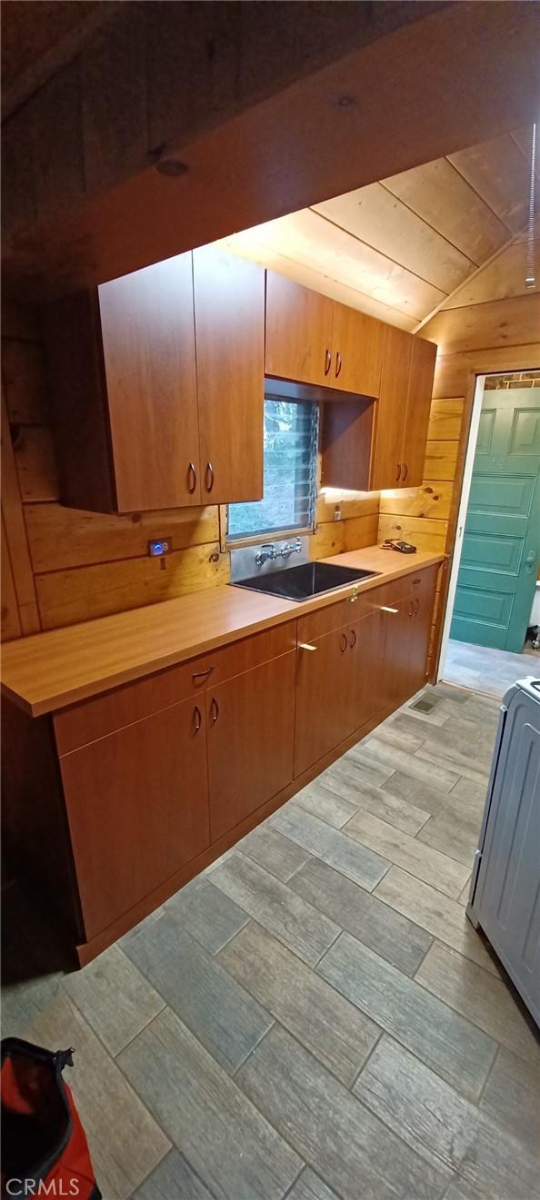 kitchen featuring butcher block counters, light hardwood / wood-style floors, wooden walls, lofted ceiling, and sink