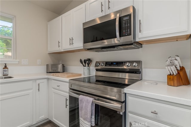 kitchen with appliances with stainless steel finishes, white cabinetry, vaulted ceiling, and sink