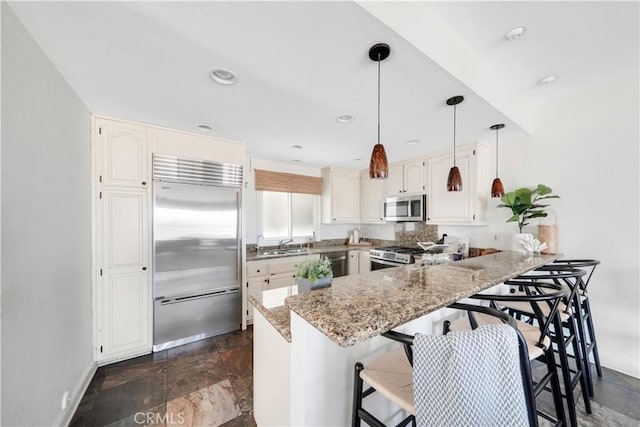 kitchen with light stone counters, stone finish floor, baseboards, a peninsula, and appliances with stainless steel finishes