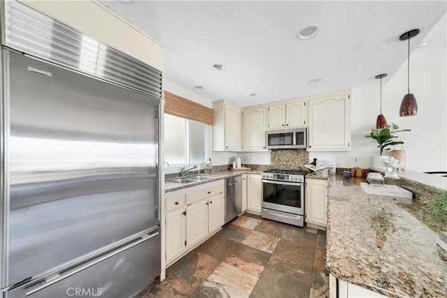 kitchen with sink, appliances with stainless steel finishes, decorative light fixtures, light stone counters, and kitchen peninsula