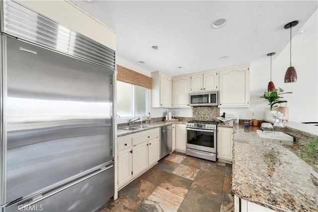 kitchen with light stone counters, a sink, hanging light fixtures, appliances with stainless steel finishes, and stone finish floor