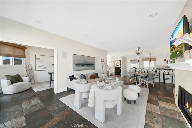 living room with a glass covered fireplace, a wealth of natural light, and stone tile flooring