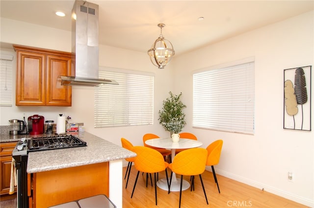 kitchen with hanging light fixtures, light stone countertops, island exhaust hood, light wood-type flooring, and gas range oven