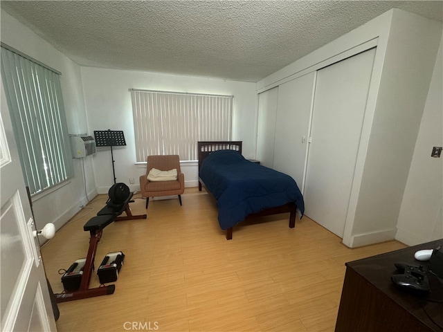 bedroom featuring a wall mounted air conditioner, a textured ceiling, light wood-type flooring, and a closet