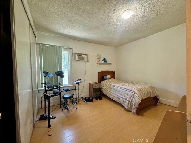 bedroom with wood-type flooring, a textured ceiling, and a wall unit AC