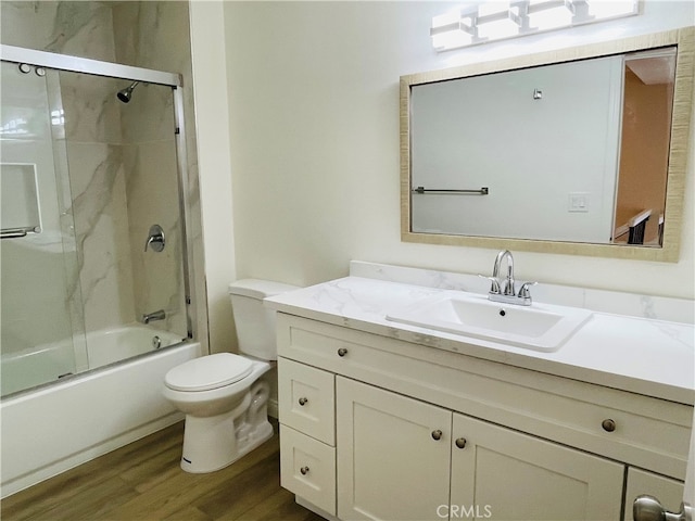 full bathroom featuring combined bath / shower with glass door, hardwood / wood-style flooring, vanity, and toilet