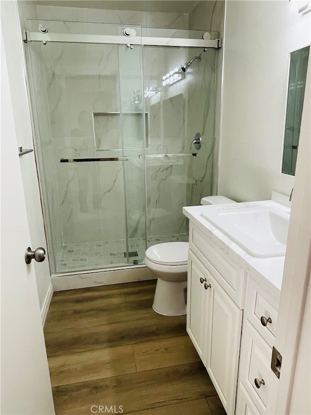 bathroom featuring hardwood / wood-style flooring, walk in shower, vanity, and toilet