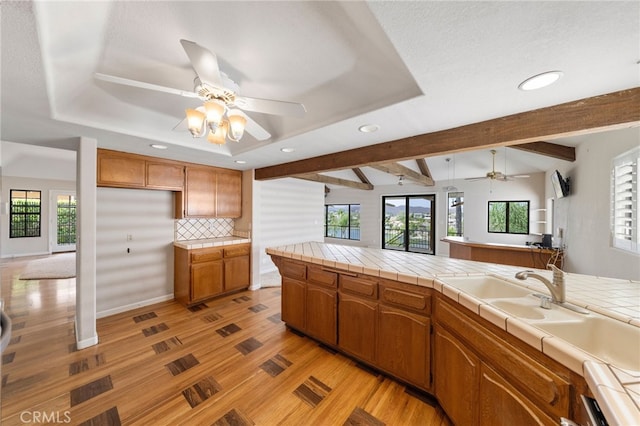 kitchen featuring tile countertops, vaulted ceiling with beams, light hardwood / wood-style floors, and backsplash