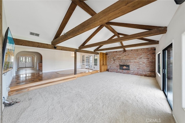 unfurnished living room featuring brick wall, light colored carpet, beam ceiling, high vaulted ceiling, and a fireplace