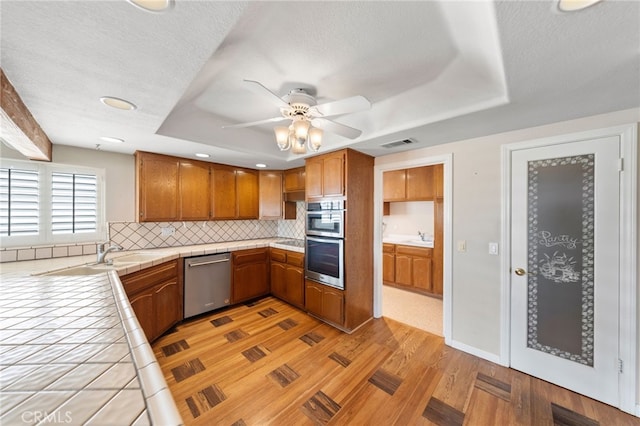 kitchen featuring stainless steel appliances, tasteful backsplash, tile countertops, light hardwood / wood-style floors, and a textured ceiling