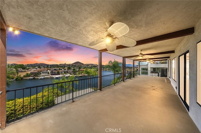 patio terrace at dusk featuring a water view, ceiling fan, and a balcony