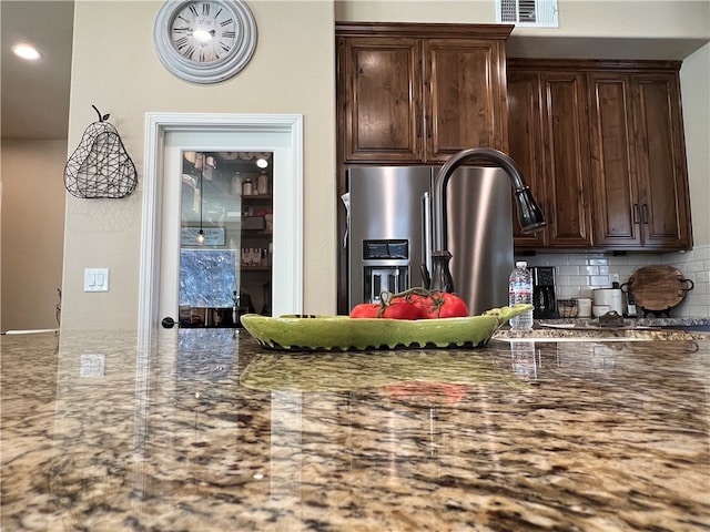 kitchen featuring stone countertops, tasteful backsplash, dark brown cabinets, and stainless steel fridge with ice dispenser