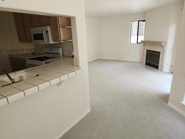 kitchen with white appliances, tile countertops, light carpet, and a tiled fireplace