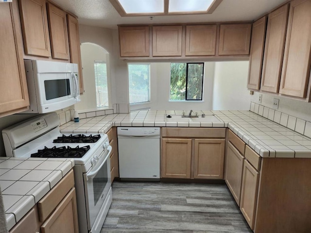 kitchen with white appliances, tile countertops, kitchen peninsula, and light hardwood / wood-style floors