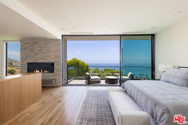 bedroom with floor to ceiling windows, light hardwood / wood-style flooring, a large fireplace, and a water view