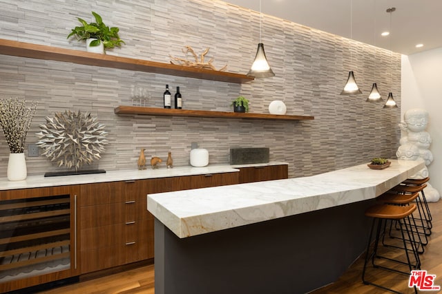 bar featuring wine cooler, tasteful backsplash, tile walls, light wood-type flooring, and decorative light fixtures