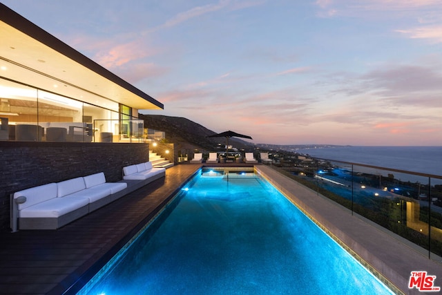 pool at dusk with a water view and outdoor lounge area