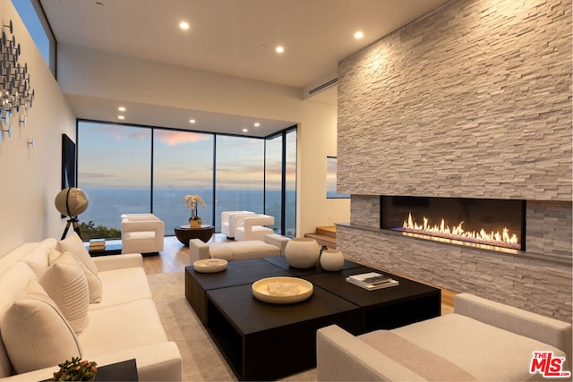 living room featuring light hardwood / wood-style flooring, a water view, floor to ceiling windows, and a fireplace