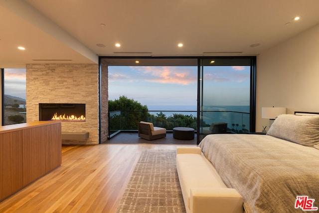 bedroom featuring expansive windows, a stone fireplace, access to exterior, and light wood-type flooring