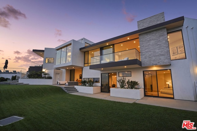 back house at dusk with a yard, a patio, and a balcony