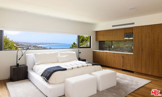 bedroom with sink, light hardwood / wood-style flooring, and a water view