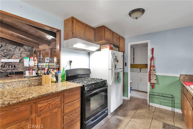 kitchen featuring gas stove, beam ceiling, light stone countertops, washing machine and dryer, and light tile patterned flooring