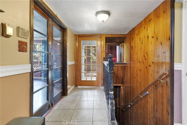 entryway with a healthy amount of sunlight, light tile patterned flooring, wooden walls, and french doors