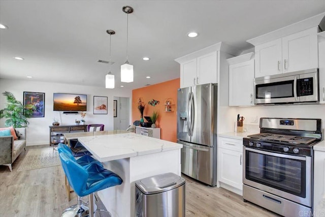 kitchen featuring appliances with stainless steel finishes, pendant lighting, light hardwood / wood-style floors, light stone countertops, and white cabinetry