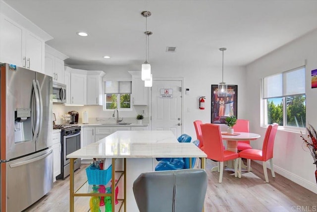 kitchen with light hardwood / wood-style flooring, a healthy amount of sunlight, pendant lighting, and stainless steel appliances