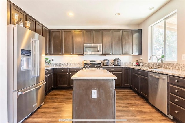 kitchen featuring dark wood-type flooring, stainless steel appliances, dark brown cabinets, a center island, and sink