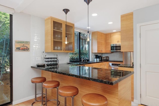 kitchen featuring dark stone countertops, appliances with stainless steel finishes, decorative light fixtures, kitchen peninsula, and a breakfast bar area