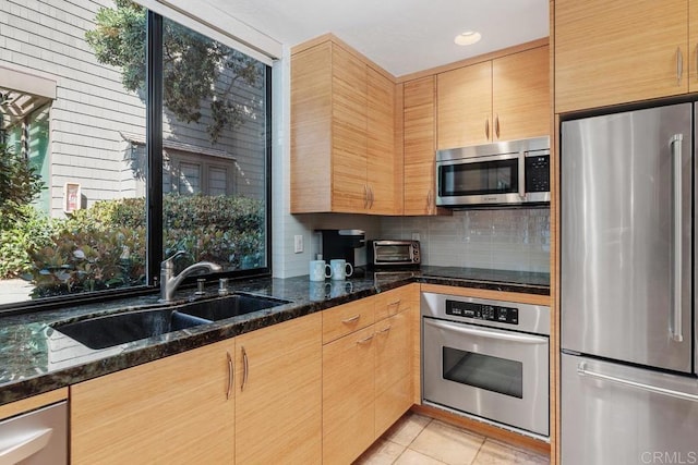 kitchen featuring sink, dark stone countertops, light tile patterned floors, appliances with stainless steel finishes, and tasteful backsplash