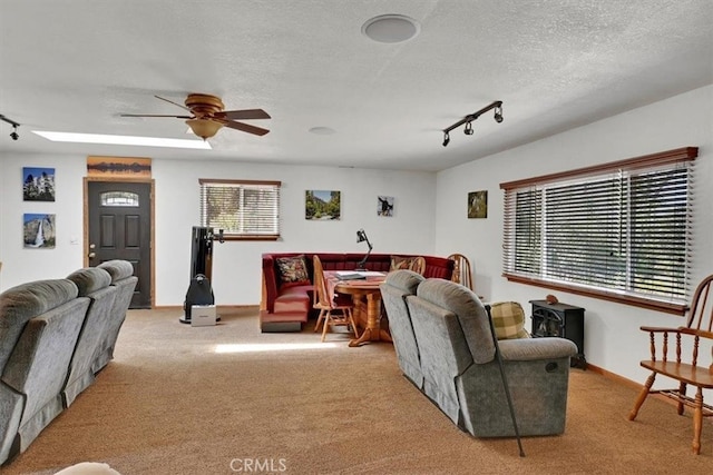 carpeted living room with a textured ceiling, rail lighting, ceiling fan, and a wealth of natural light