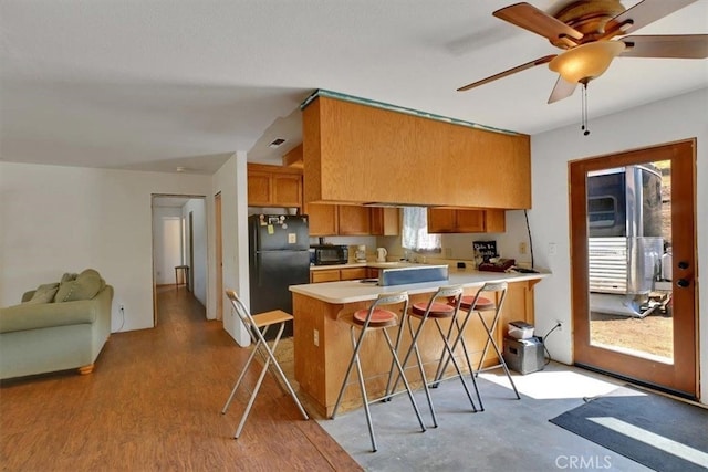 kitchen with light wood-type flooring, kitchen peninsula, a kitchen bar, black appliances, and ceiling fan