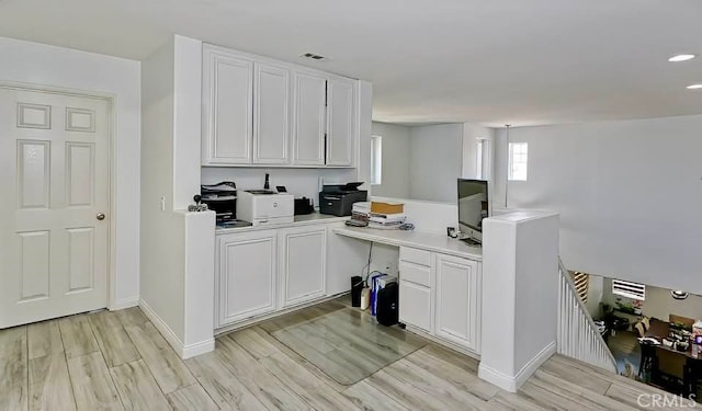 kitchen with white cabinetry, built in desk, and light hardwood / wood-style floors