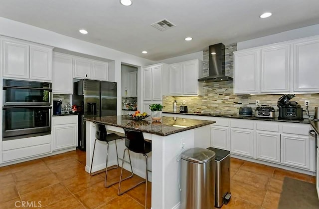 kitchen with black appliances, white cabinetry, a center island, and wall chimney exhaust hood