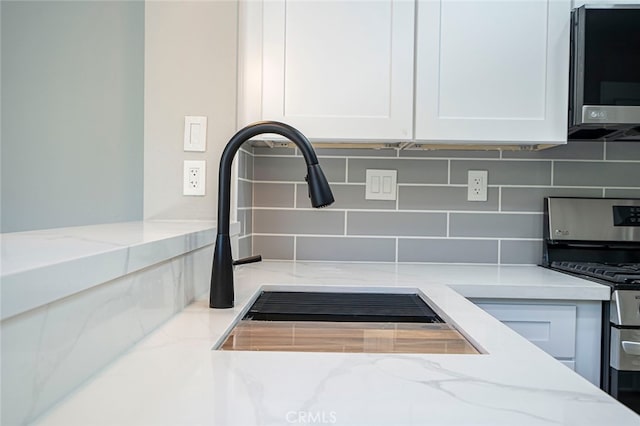 interior details featuring white cabinets, light stone counters, stainless steel appliances, and tasteful backsplash