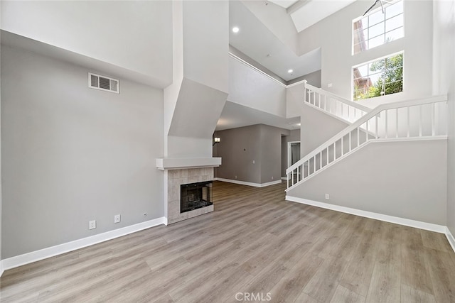 unfurnished living room featuring a tiled fireplace, light hardwood / wood-style floors, and a high ceiling