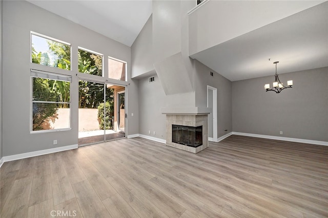 unfurnished living room featuring a healthy amount of sunlight, light hardwood / wood-style floors, a notable chandelier, and a fireplace